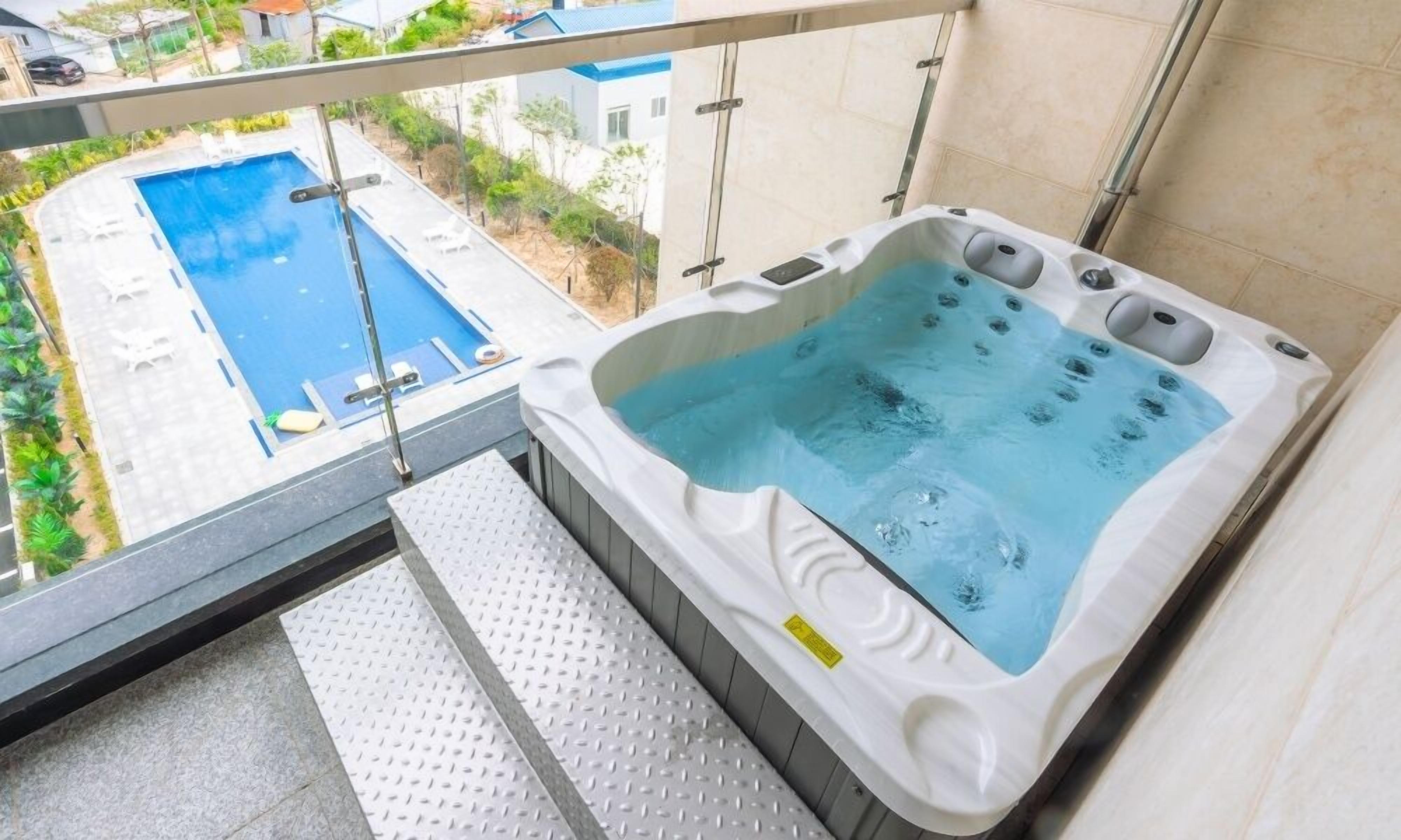 Uma banheira de hidromassagem com vista para uma piscina e uma varanda com guarda-corpo de metal.