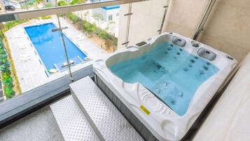 Uma banheira de hidromassagem com vista para uma piscina e uma varanda com guarda-corpo de metal.