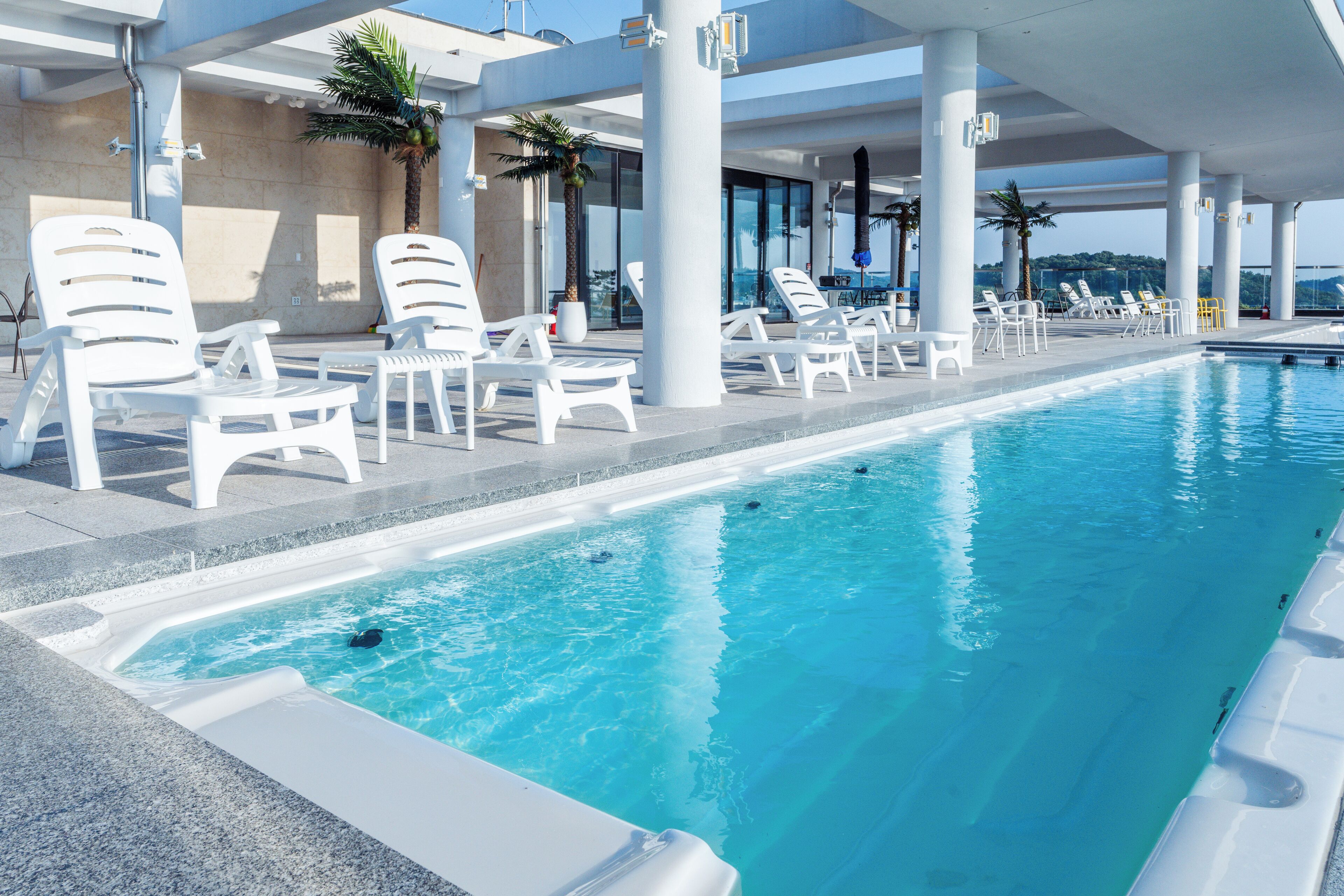A swimming pool with white lounge chairs and palm trees.