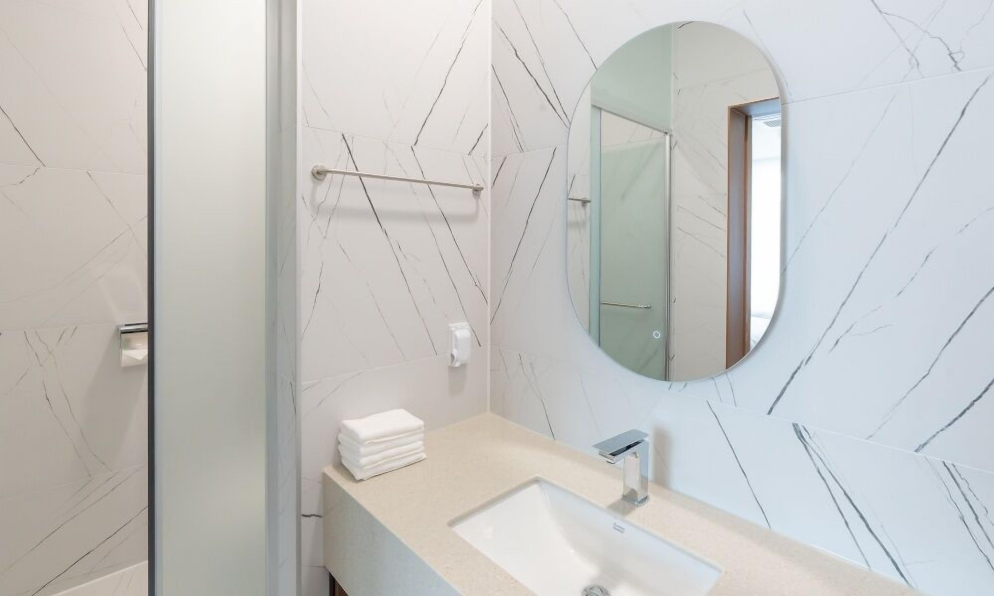 A modern bathroom with a marble wall, a round mirror, a sink, and a towel rack.
