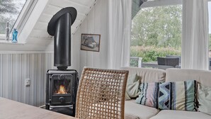 Ett mysigt vardagsrum med en vedeldad kamin, en flätstol och en soffa med mönstrade kuddar.