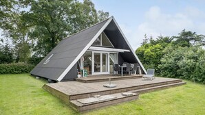 Ett modernt hus i A-formsstil med en träveranda, en matplats och en uteplats med utemöbler.