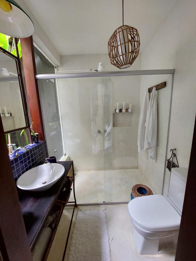 Casa de banho com cabine de duche em vidro, lavatório branco e sanita.