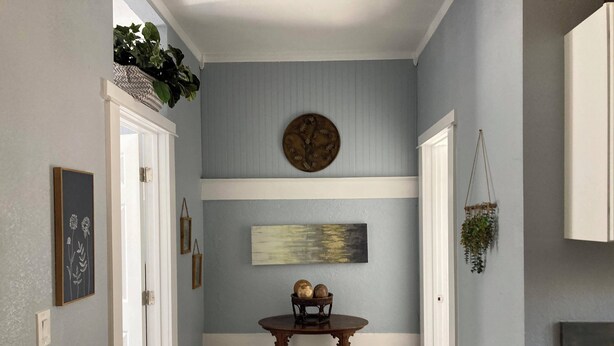 A hallway with a blue wall, a wooden table with a basket, and a hanging plant.