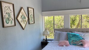 A bedroom with a bed, a ceiling fan, an air conditioner, and two windows.