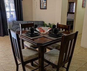 Un coin repas avec une table et des chaises en bois, un vase en verre servant de centre de table, et un canapé gris en arrière-plan.