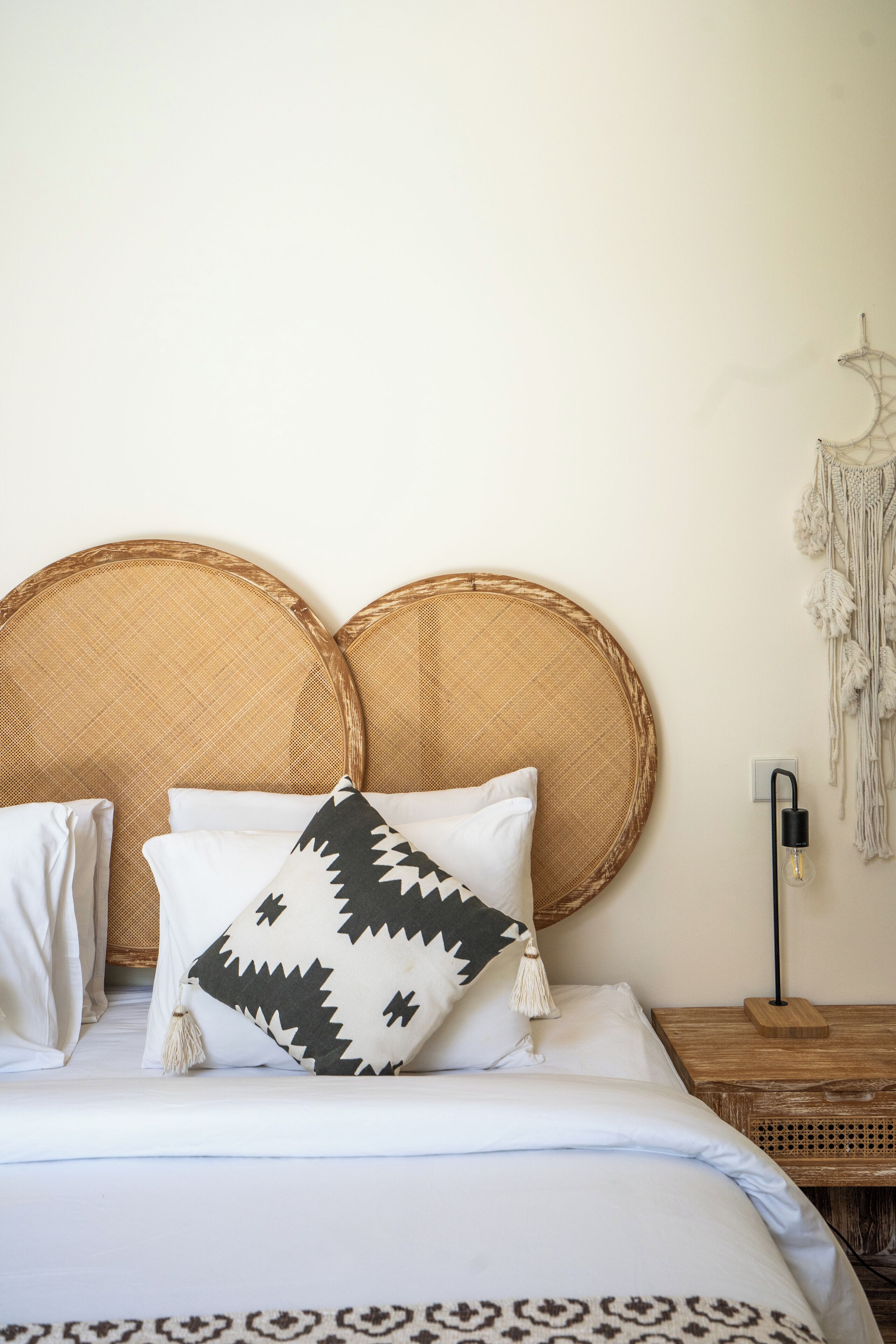 A bed with a woven headboard, white bedding, and a macrame wall hanging.