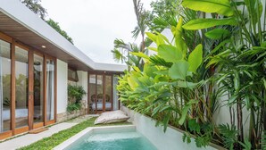 A modern house with a swimming pool, large windows, and lush tropical plants. - Gaia Villa by Betterplace (Canggu)