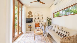 A living room with a sofa, a coffee table, a TV, and a ceiling fan. - Gaia Villa by Betterplace (Canggu)