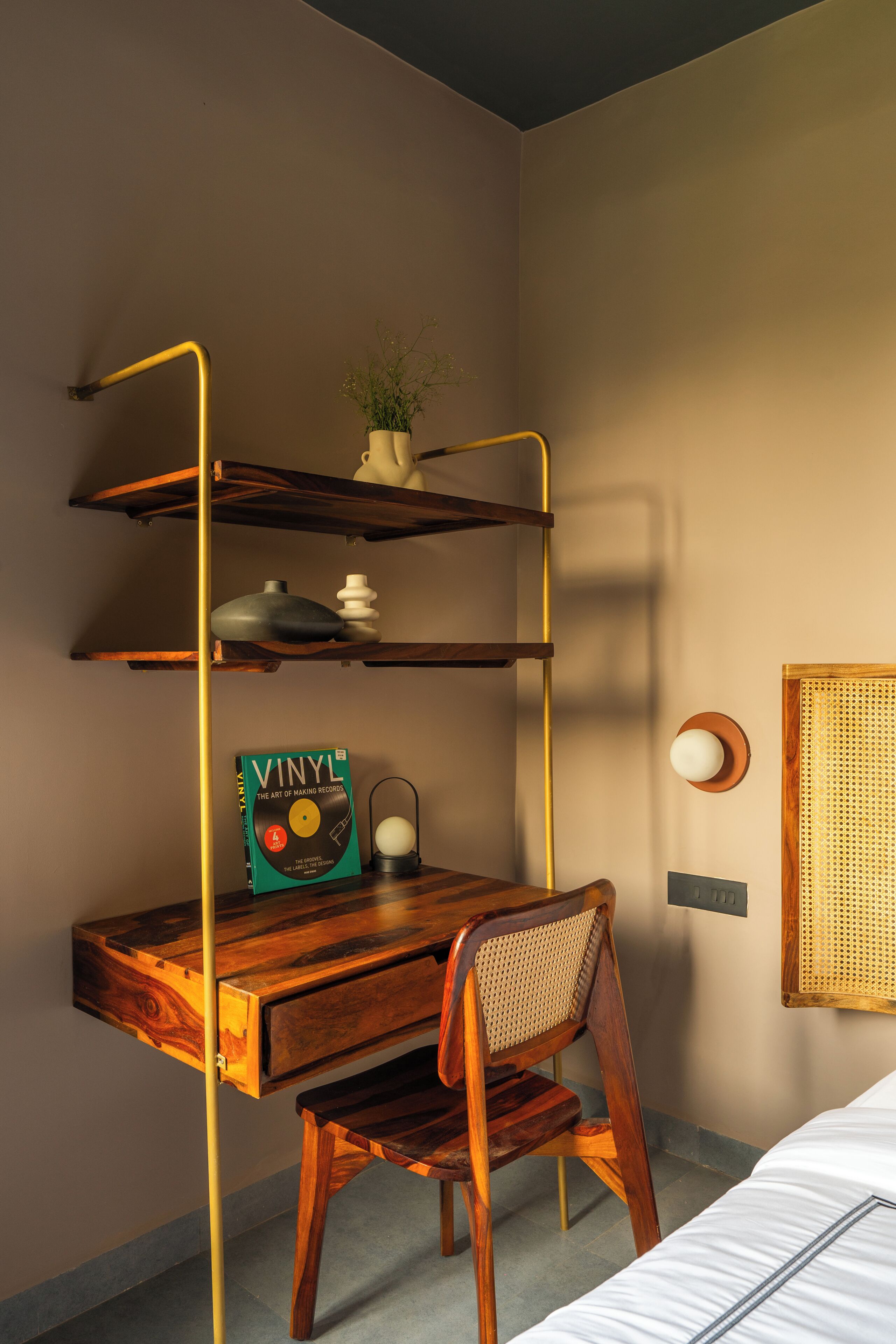 A compact room with a wooden desk, a chair, a bookshelf, and a wall-mounted lamp.