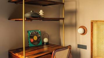 A compact room with a wooden desk, a chair, a bookshelf, and a wall-mounted lamp.