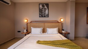 A hotel room with a large bed, two bedside tables, a wall-mounted air conditioner, and a framed artwork above the bed. - Minimalist Panjim (Panaji)