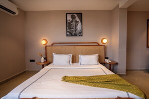A hotel room with a large bed, two bedside tables, a wall-mounted air conditioner, and a framed artwork above the bed. - Minimalist Panjim (Panaji)