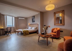 A hotel room with a bed, a desk, a chair, a round coffee table, and a large mirror. - Minimalist Panjim (Panaji)