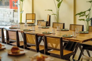 A dining area with a long wooden table set for a meal, surrounded by wicker chairs. - Minimalist Panjim (Panaji)