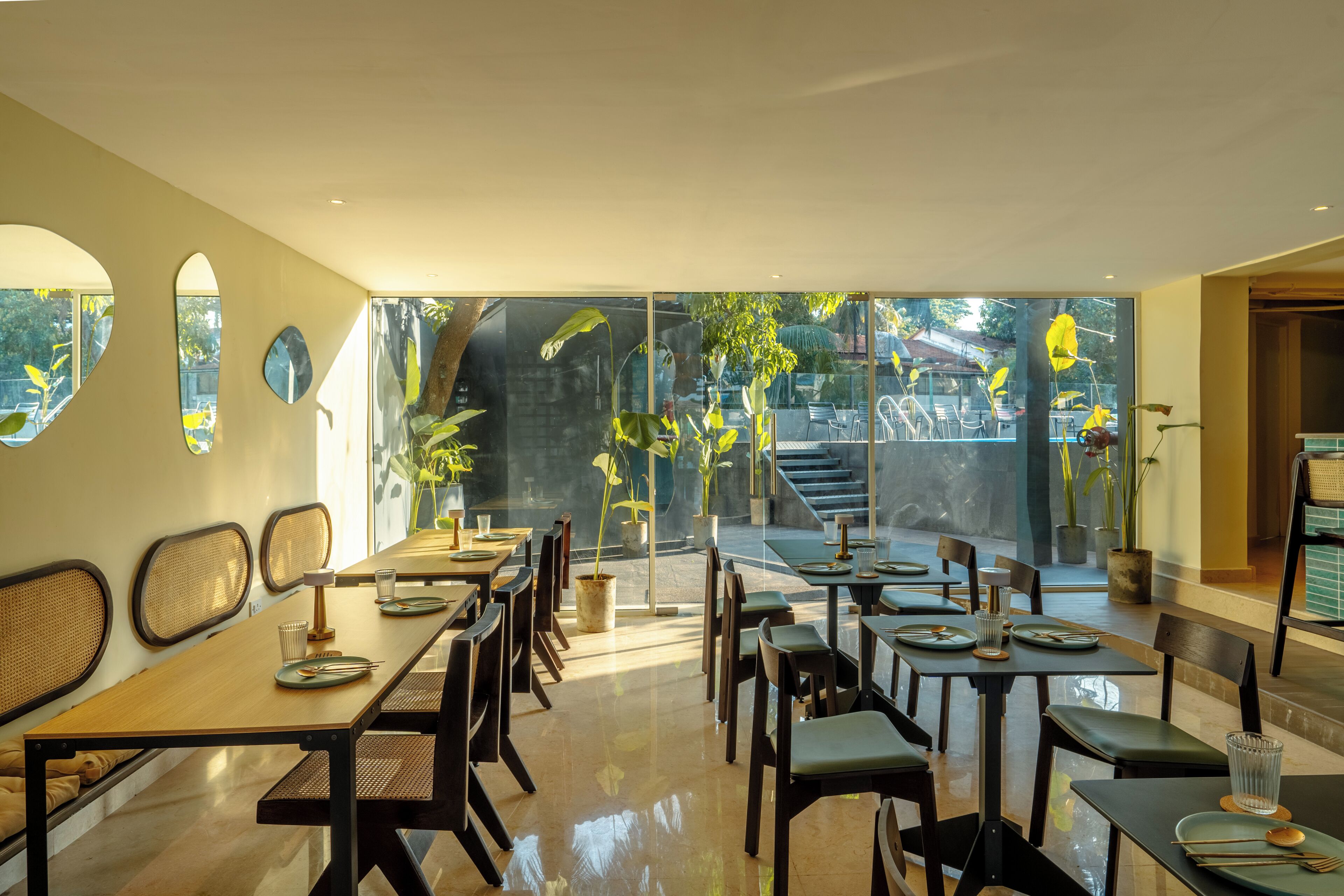 A restaurant with a modern interior, featuring a long dining table, chairs, and potted plants.