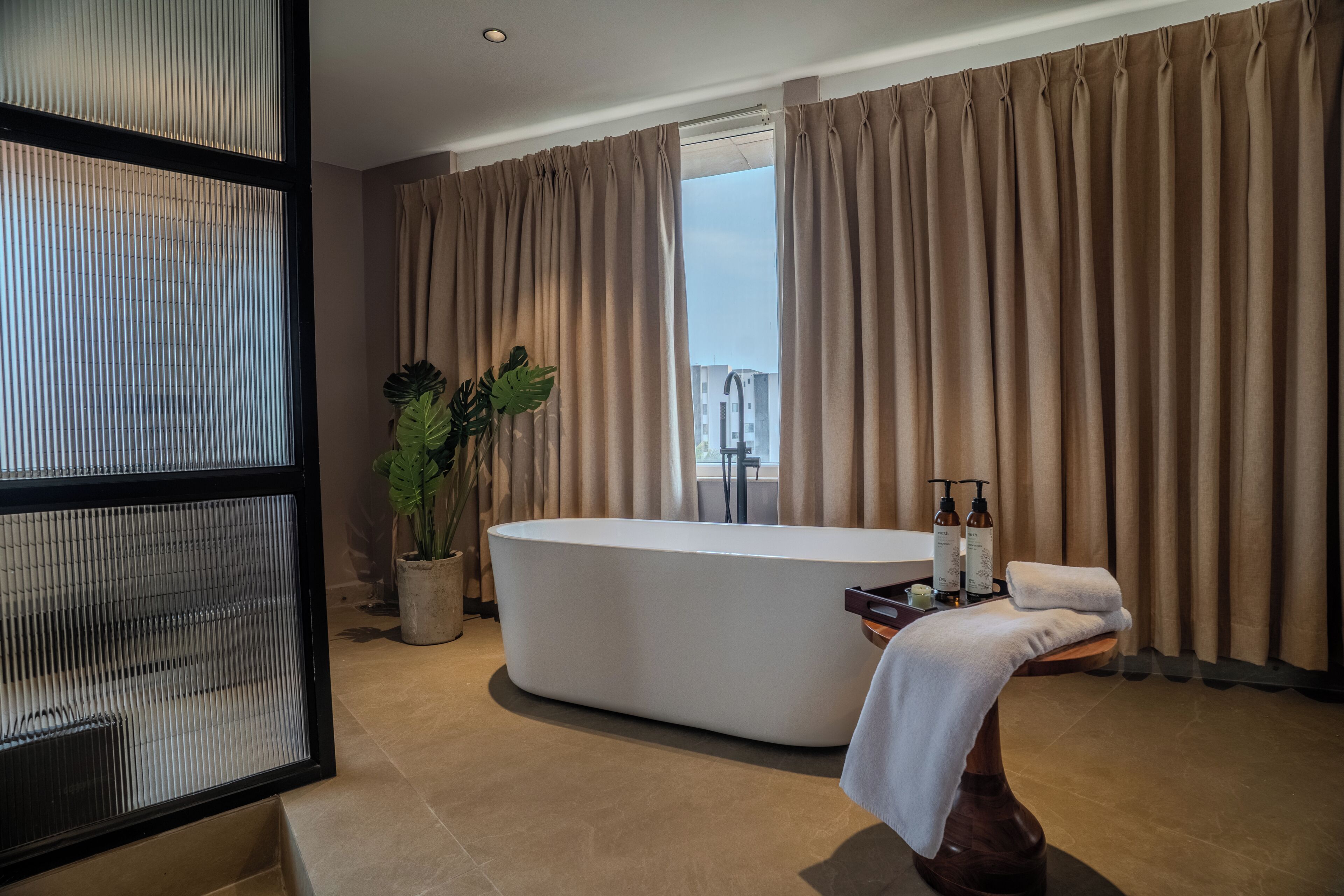 Un baño moderno con una bañera independiente, una planta en maceta y artículos de aseo en una mesita.