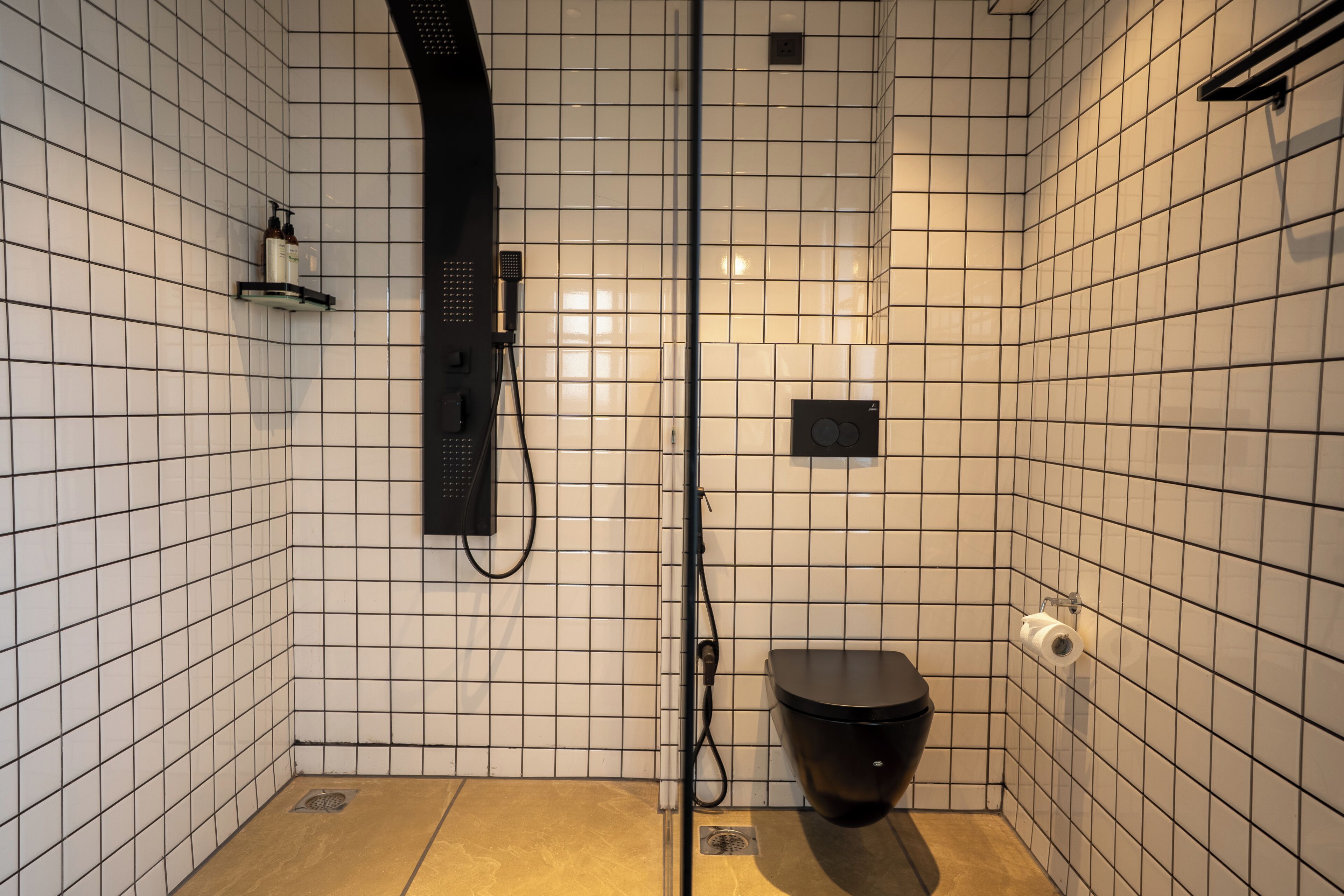 Un baño pequeño con azulejos, ducha, inodoro y un estante con artículos de aseo.