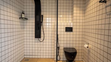 Ein kleines Badezimmer mit Fliesen, einer Dusche, einer Toilette und einem Ablagefach für Toilettenartikel.