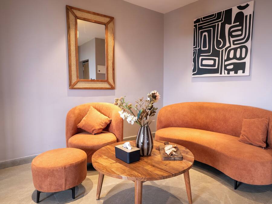 A living room with two orange sofas, a round coffee table, a small ottoman, a mirror, and a wall art piece.