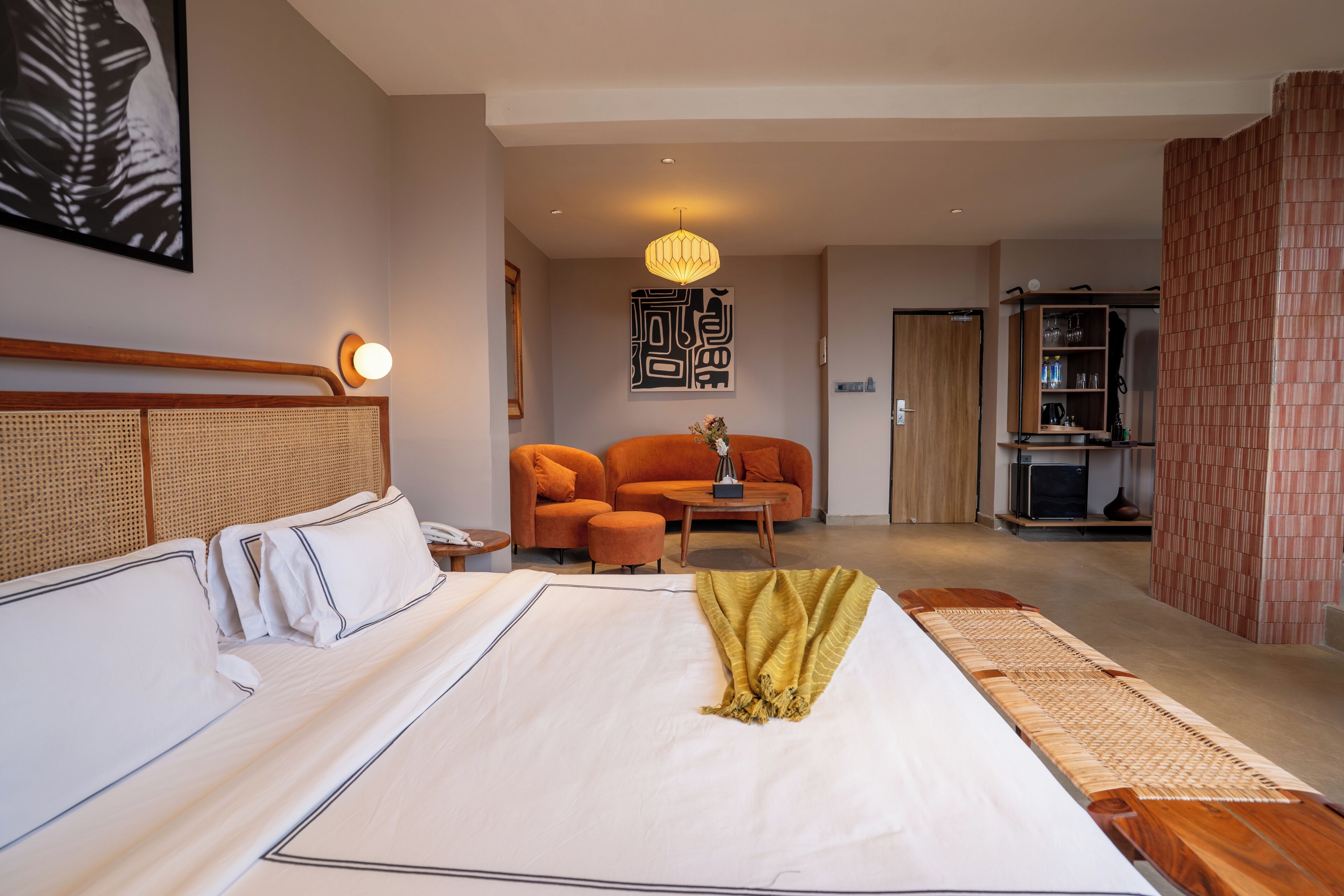 A hotel room with a large bed, a sofa, a small table, and a hanging light fixture.