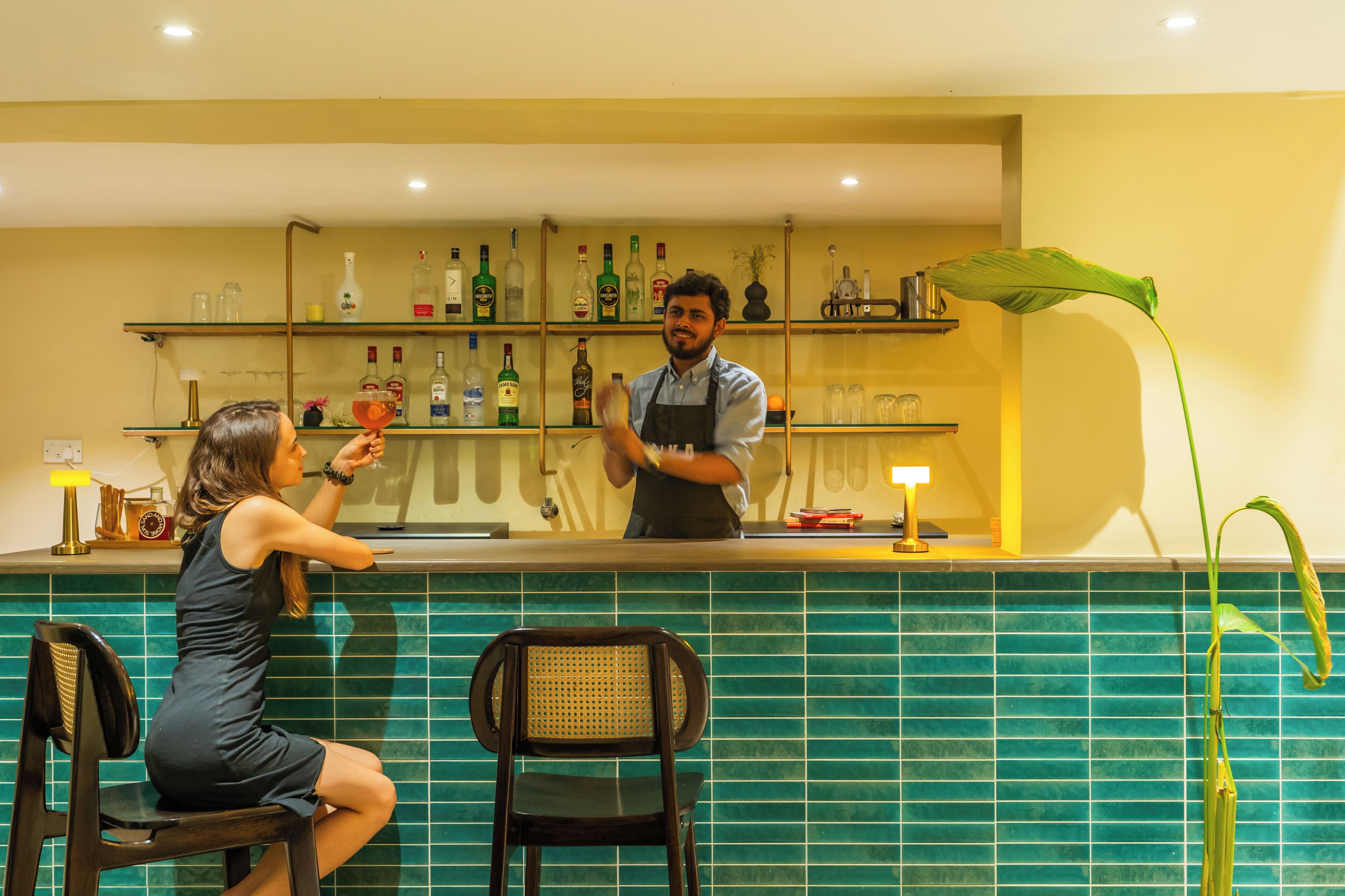 A bar area with a bartender and a customer. There are shelves with bottles behind the bar.