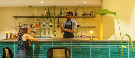 A bar area with a bartender and a customer. There are shelves with bottles behind the bar.
