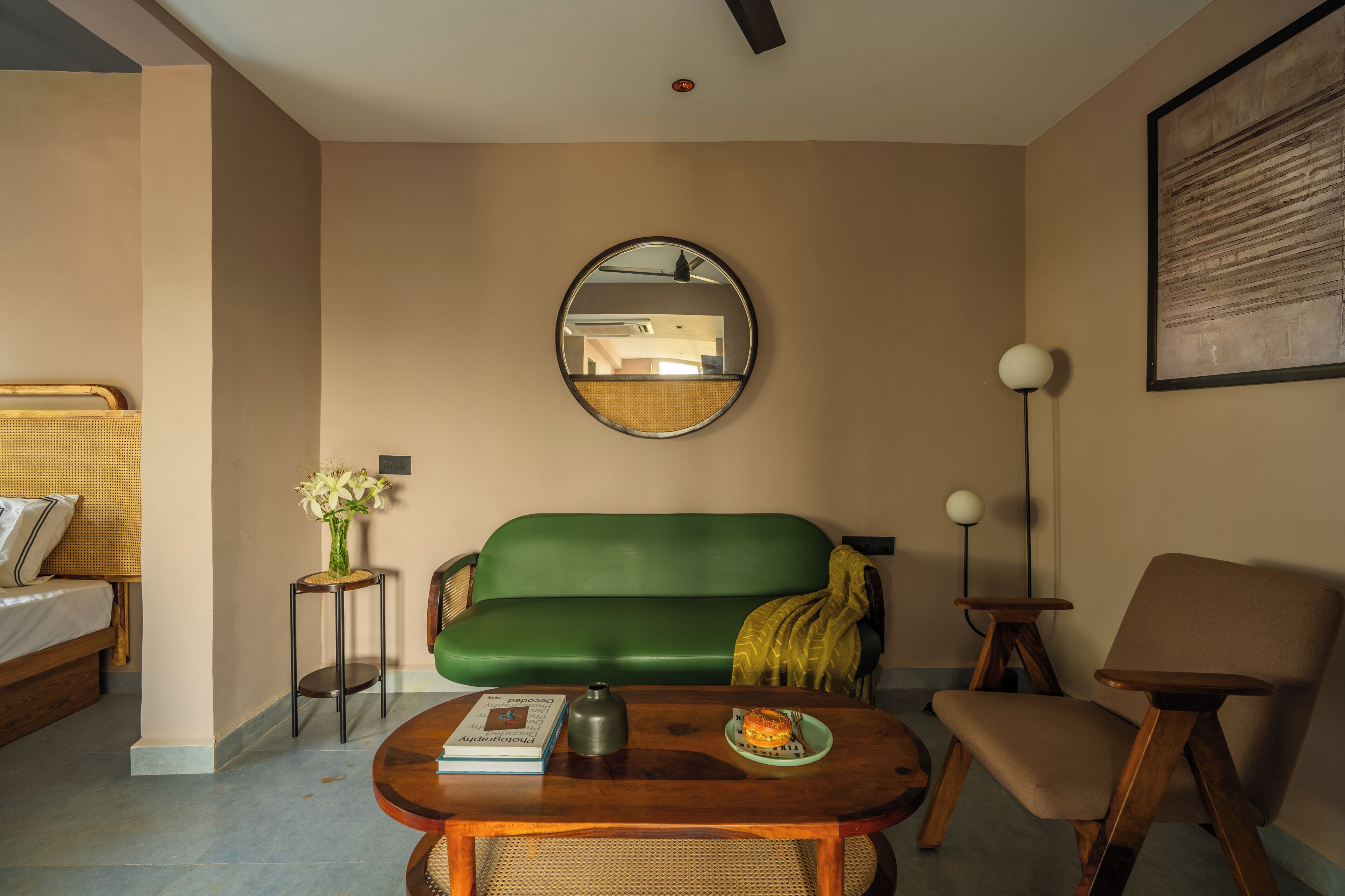Una habitación con un sofá verde, una mesa de centro de madera, una mesita auxiliar con un florero, una lámpara de pie y un cuadro en la pared.