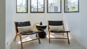 Une pièce d’angle dotée de trois grandes fenêtres, de deux chaises en bois avec des coussins et d’une table ronde agrémentée d’un objet décoratif.