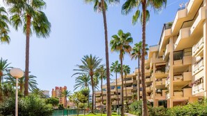 A multi-story hotel with balconies, surrounded by palm trees and a well-maintained lawn. - Montemar Puerto - Beachfront, Terrace, Swimming Pool. Sea Views (Torremolinos)