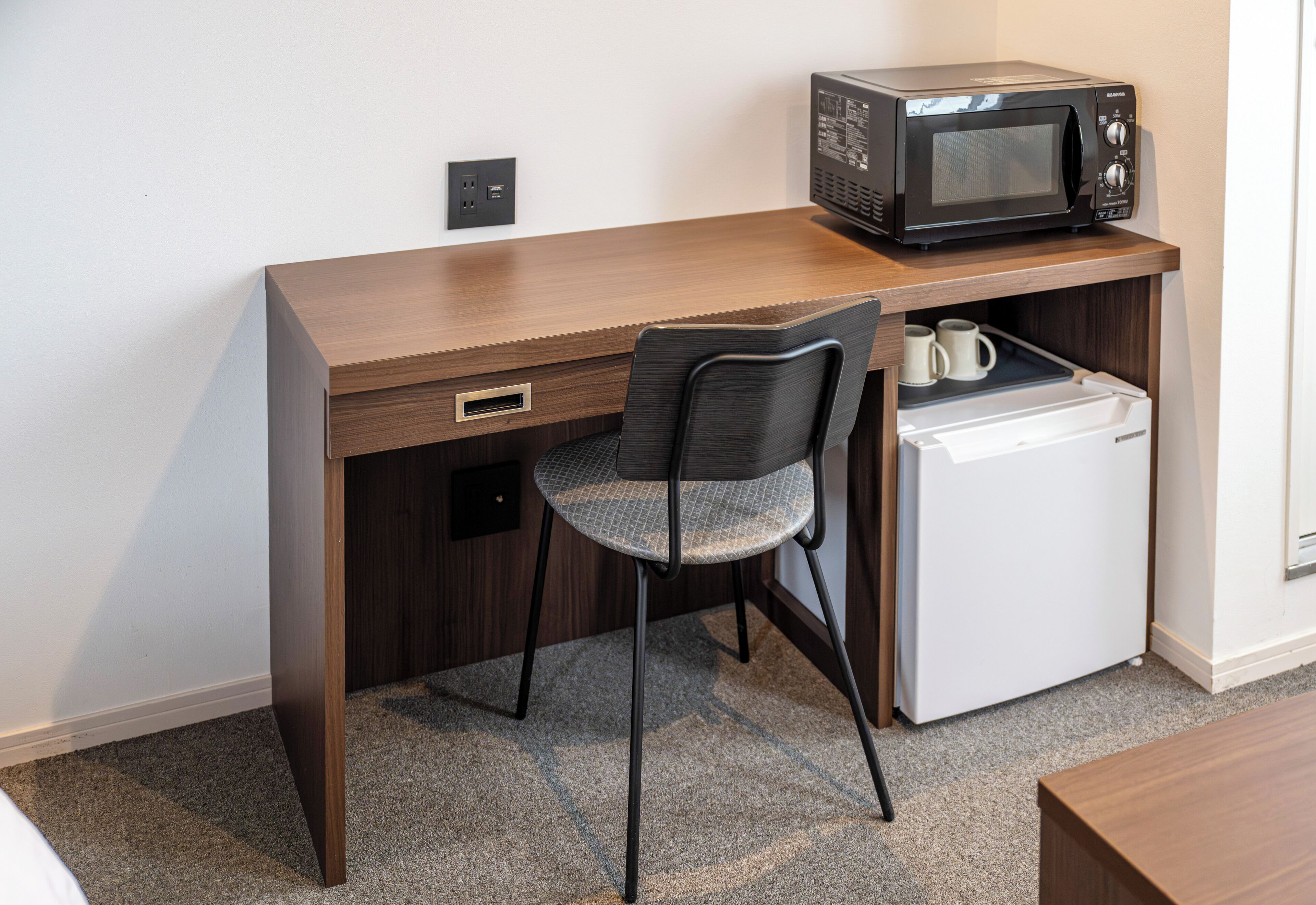 Una kitchenette compacta con microondas, un refrigerador pequeño y una silla.