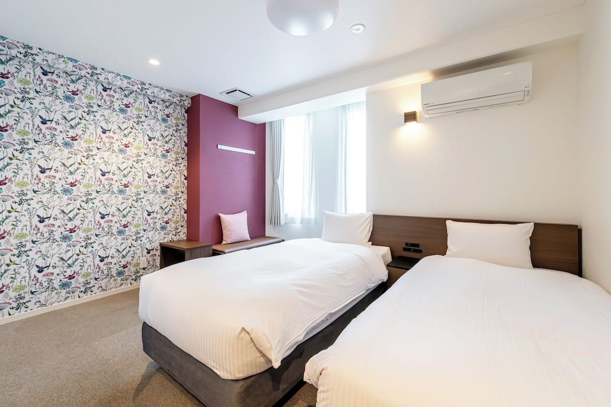 Una habitación de hotel moderna con dos camas, un ventanal grande y un papel tapiz con estampado floral.