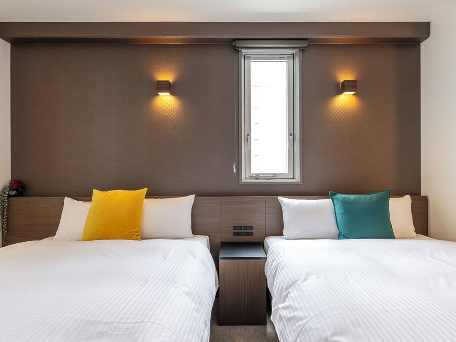 Et hotelværelse med to senge, et vindue og vægmonterede lamper.
