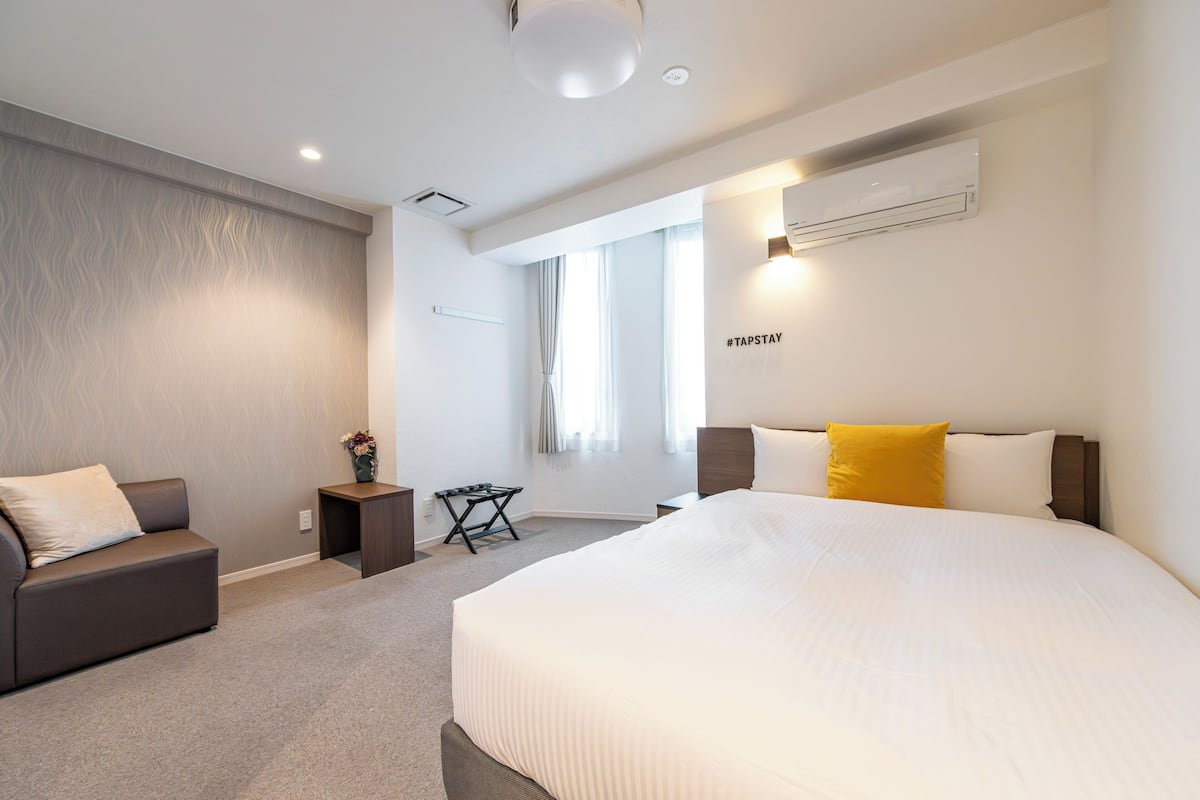 Habitación de hotel moderna con una cama grande, un sofá, una mesita y un ventanal con cortinas.