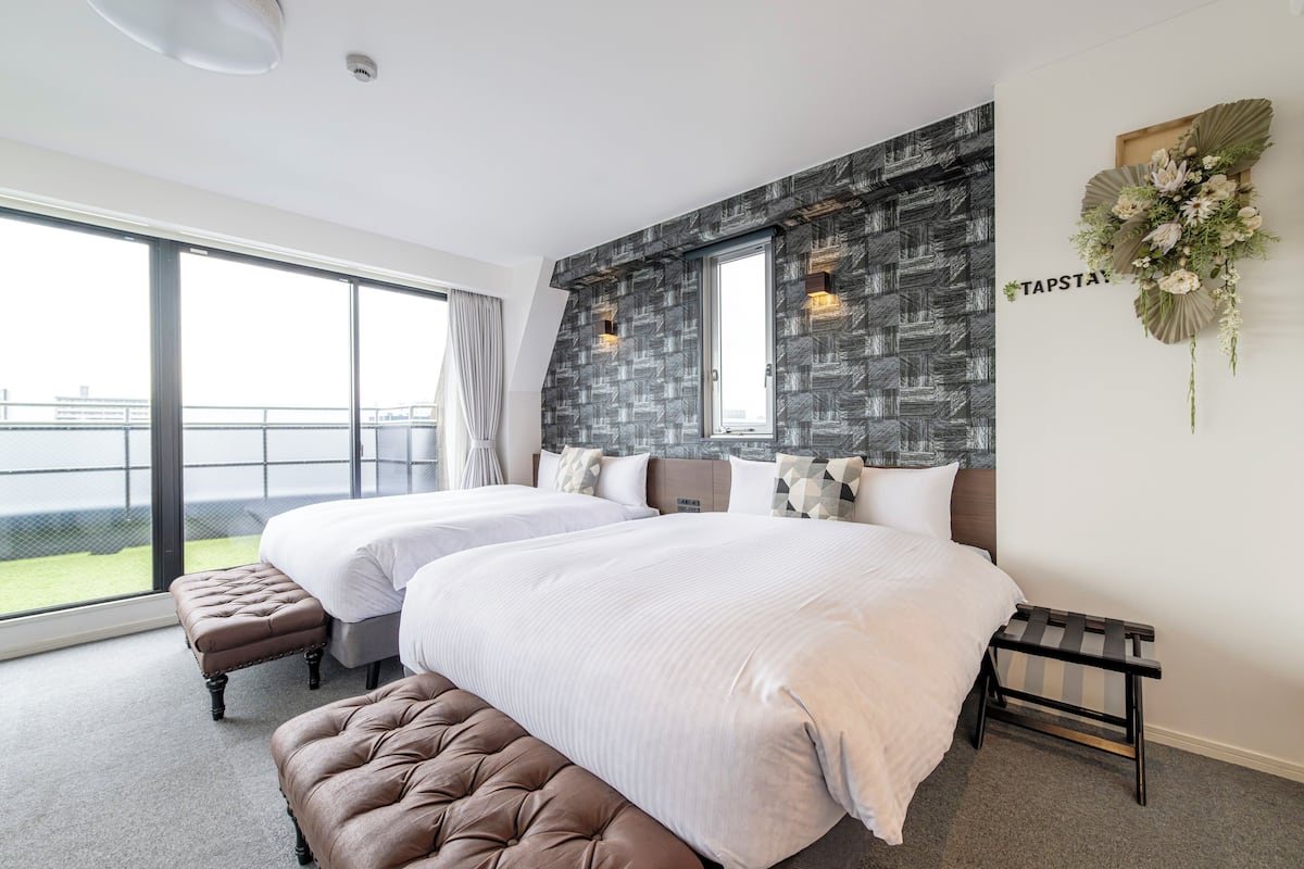 Una habitación de hotel moderna con dos camas, un ventanal grande y un balcón.