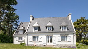 Une maison à deux étages, dotée d’une façade symétrique, de lucarnes et de fondations en pierre.