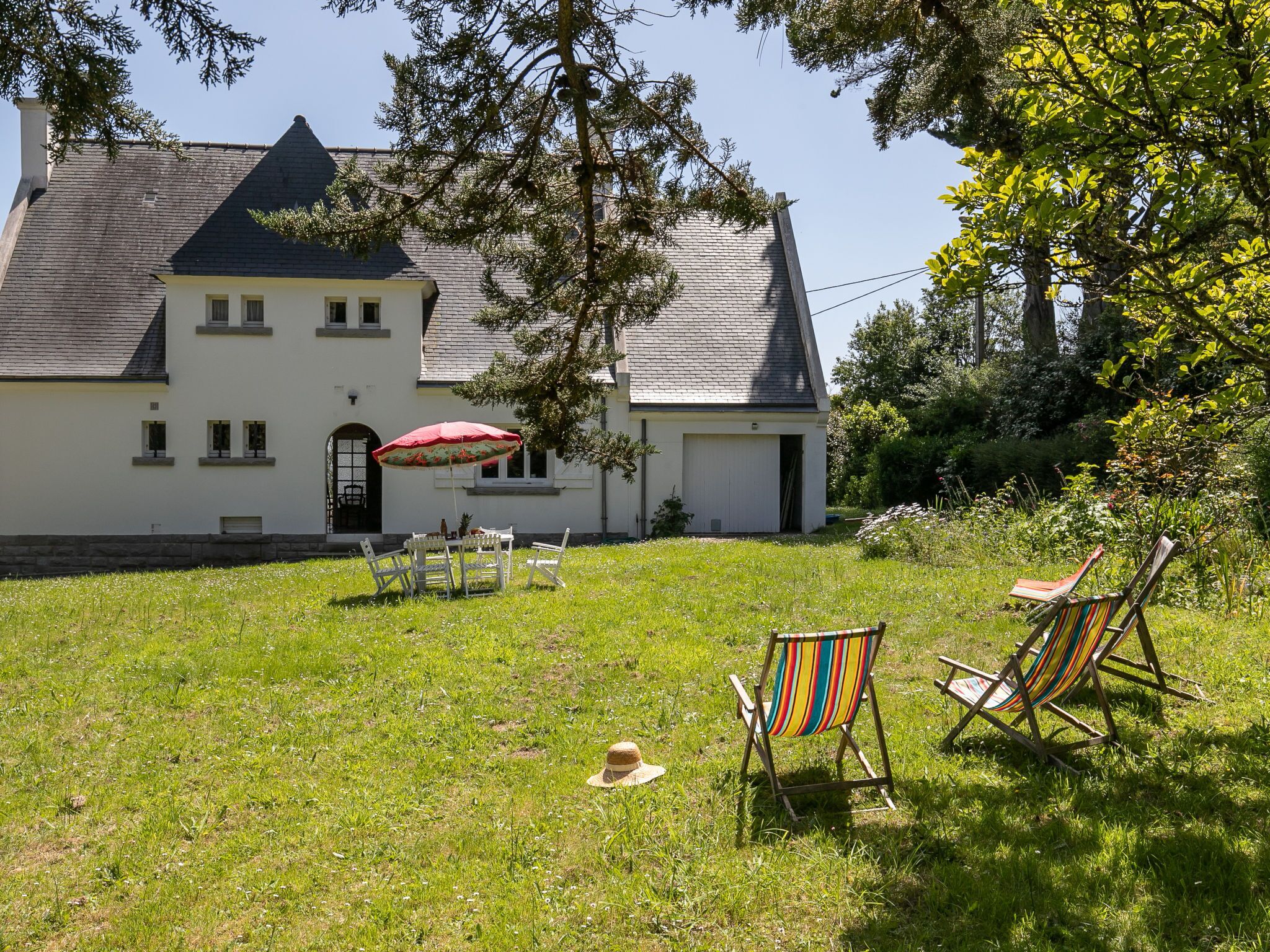 A white house with a grey roof, a patio with a table and chairs, and a red umbrella.