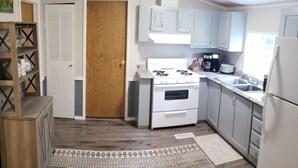 A compact kitchen with white appliances, a wooden door, and a patterned rug.
