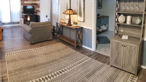 A living room with a sofa, a coffee table, a lamp, and a patterned rug. There is a TV and a fireplace in the background.