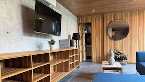 A modern living room with a flat-screen TV mounted on the wall, wooden shelves, a round mirror, and a blue sofa. - Nabani Condominios T3 (Santa María Huatulco)