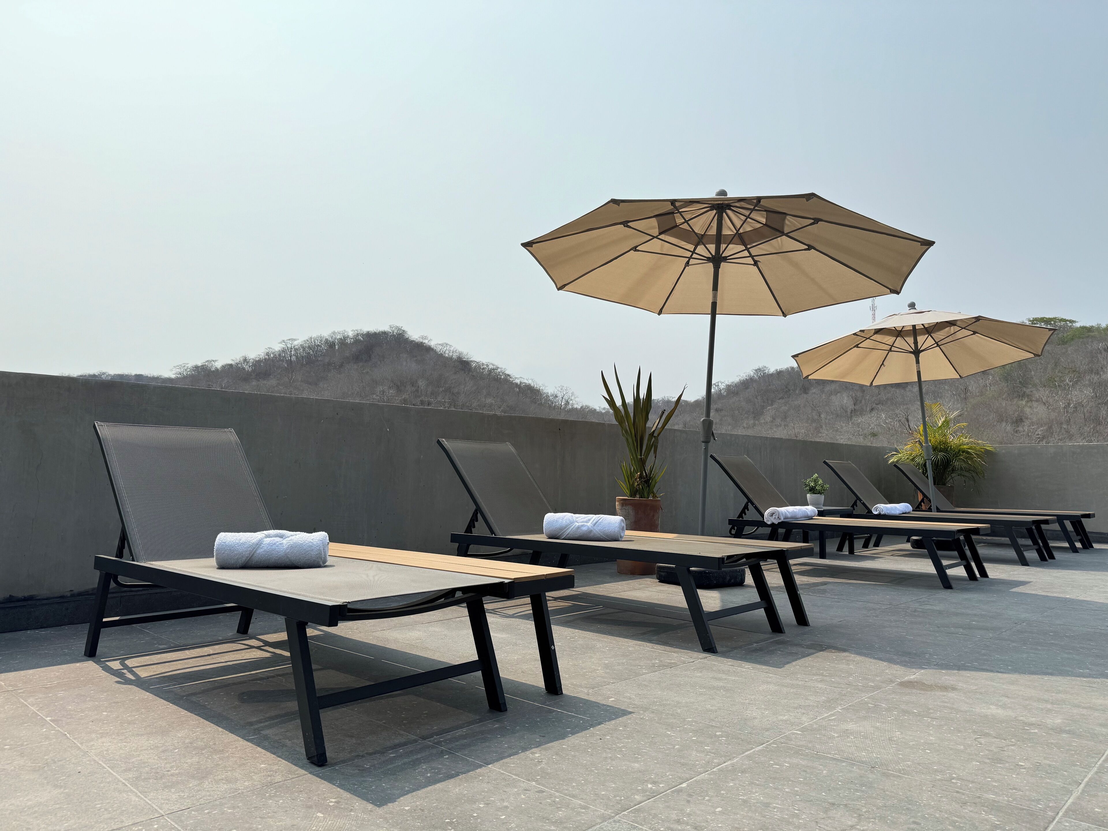Eine Dachterrasse mit Liegestühlen, Tischen und Sonnenschirmen.