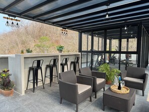 Ein überdachter Außenbereich mit Korbmöbeln, Barhocker und einer Bar.