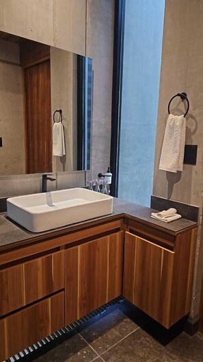 Ein modernes Badezimmer mit einem großen Waschbecken, Holzsärchen, einem Spiegel und einem Fenster.