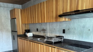 A modern kitchen with wooden cabinets, a stainless steel refrigerator, a black countertop, and a built-in stove. - Nabani Condominios T3 (Santa María Huatulco)