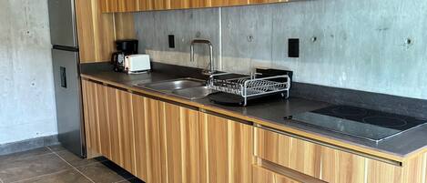 A modern kitchen with wooden cabinets, a stainless steel refrigerator, a black countertop, and a built-in stove.