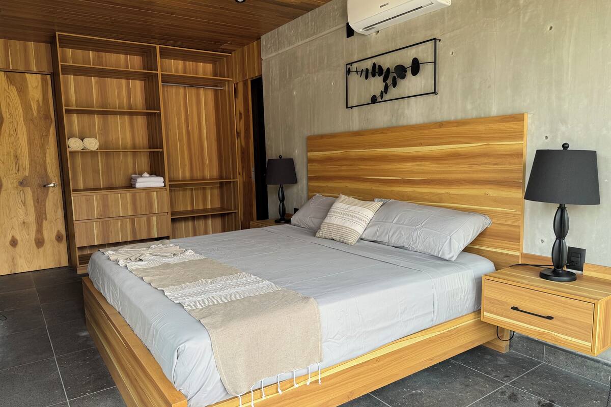 Un dormitorio con cama de madera, mesita de noche, armario y aire acondicionado instalado en la pared.