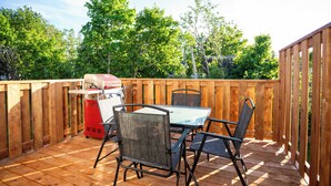 An outdoor patio with a wooden deck, a table, and chairs.