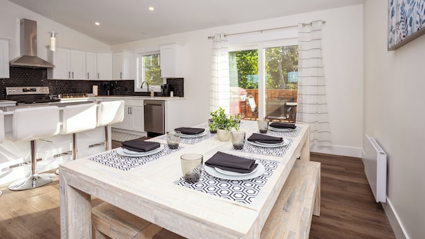 A modern kitchen with white cabinets, a black backsplash, and a dining area with a patterned tablecloth.