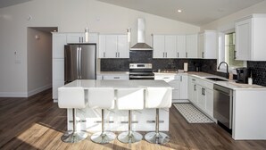 A modern kitchen with white cabinetry, a central island with bar stools, a stainless steel refrigerator, and a black backsplash.