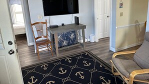 Uma sala de estar com televisão de tela plana, móveis de madeira, tapete estampado e uma porta que dá para outro cômodo.